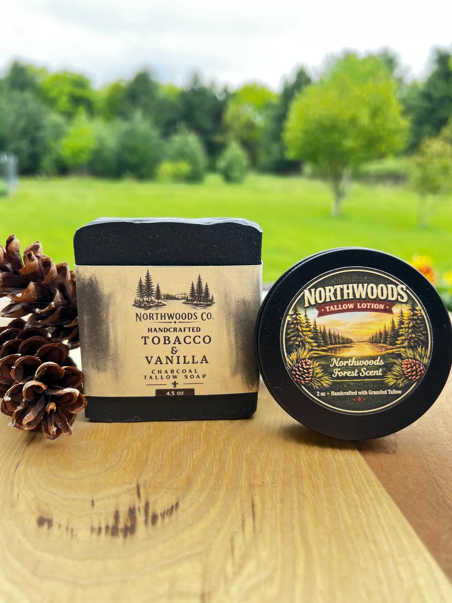 May include: A black charcoal tallow soap bar and a round tin of lotion are displayed on a wooden surface. The soap is labeled "Northwoods Co. Tobacco & Vanilla" and the lotion is "Northwoods Forest S
