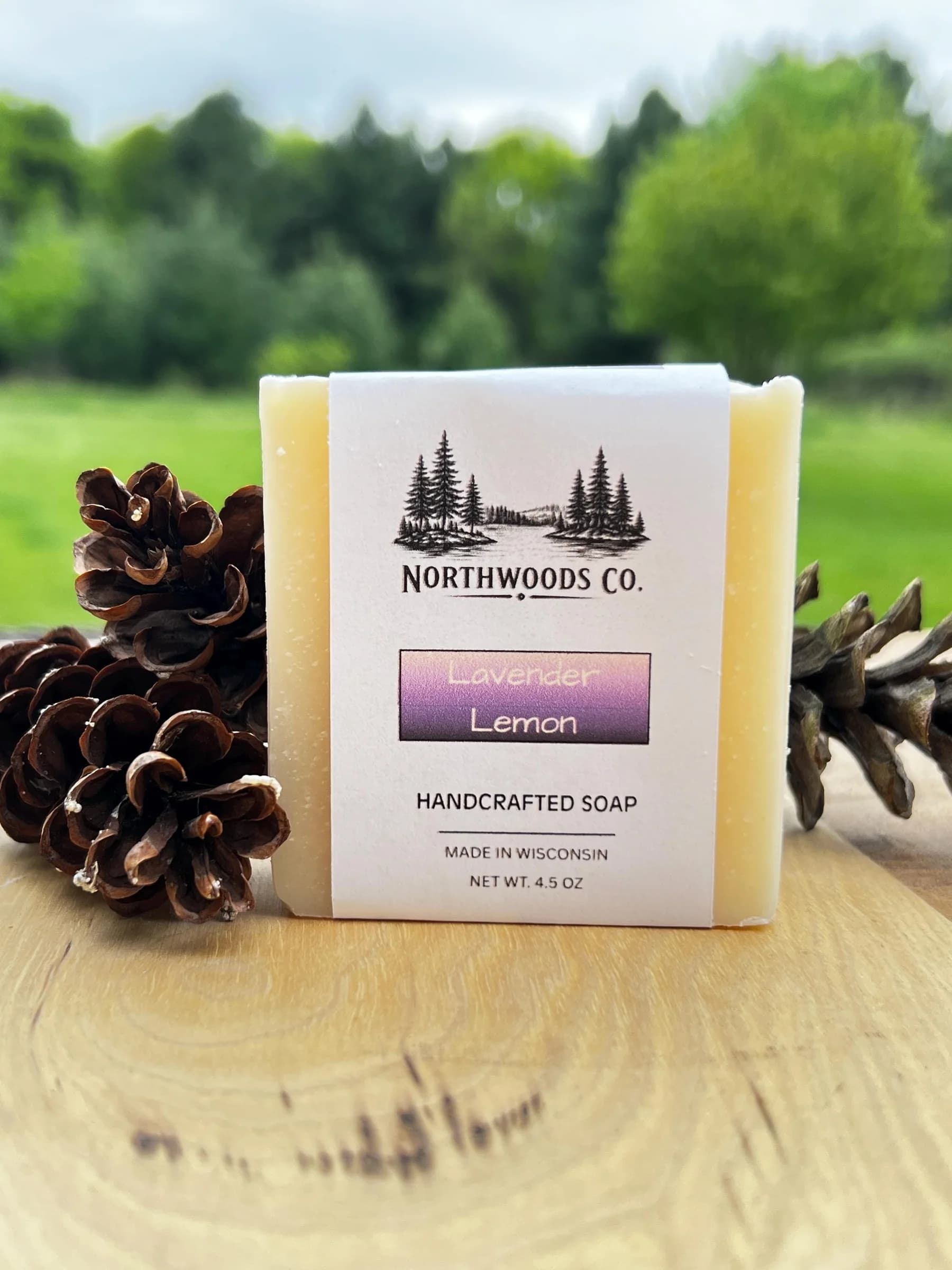 May include: A rectangular bar of handcrafted soap with a white label featuring the text "NORTHWOODS CO." and "Lavender Lemon." The soap is 4.5 oz and made in Wisconsin. The background includes pine c